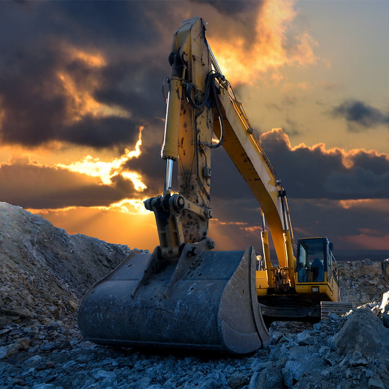 Image of a tracked excavator in a quarry with a setting sun and light rays